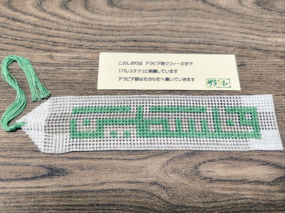 国立民族学博物館のグッズコーナーで買ったしおりと、付属の説明書きの紙。
しおりには緑色の糸によってアラビア語クフィー文字の「パレスチナ」が刺繍されている。