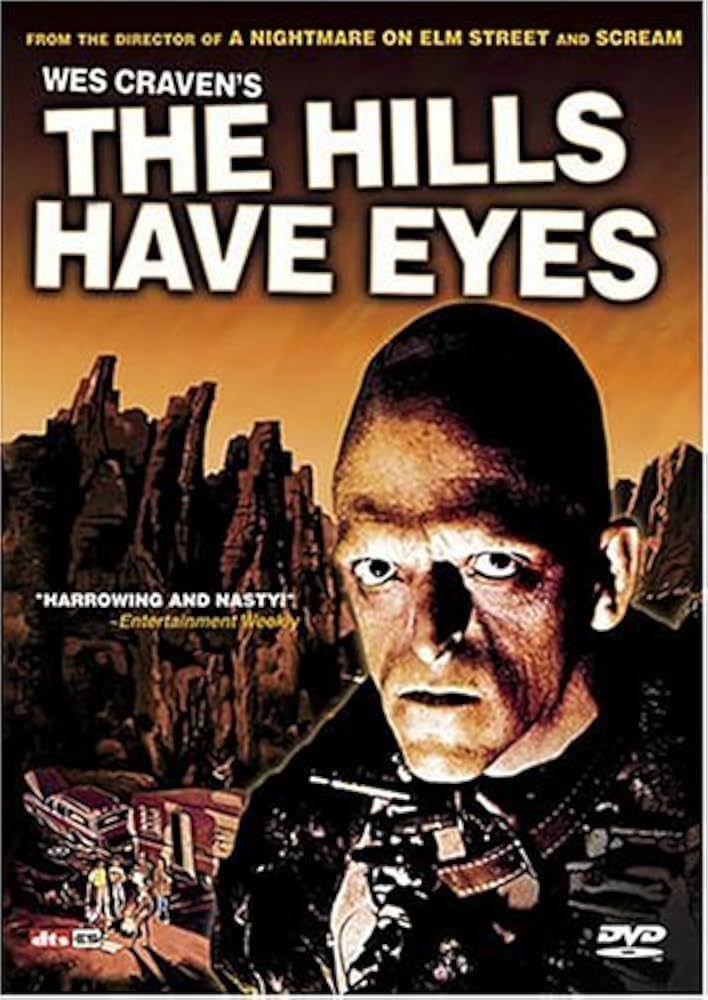Poster from The Hills Have Eyes with a menacing man with a big head stares directly out at the viewer. Background is desert at sunset with a wrecked car with a trailer and a family gathered around. The quote on the left says "Harrowing and Nasty" 