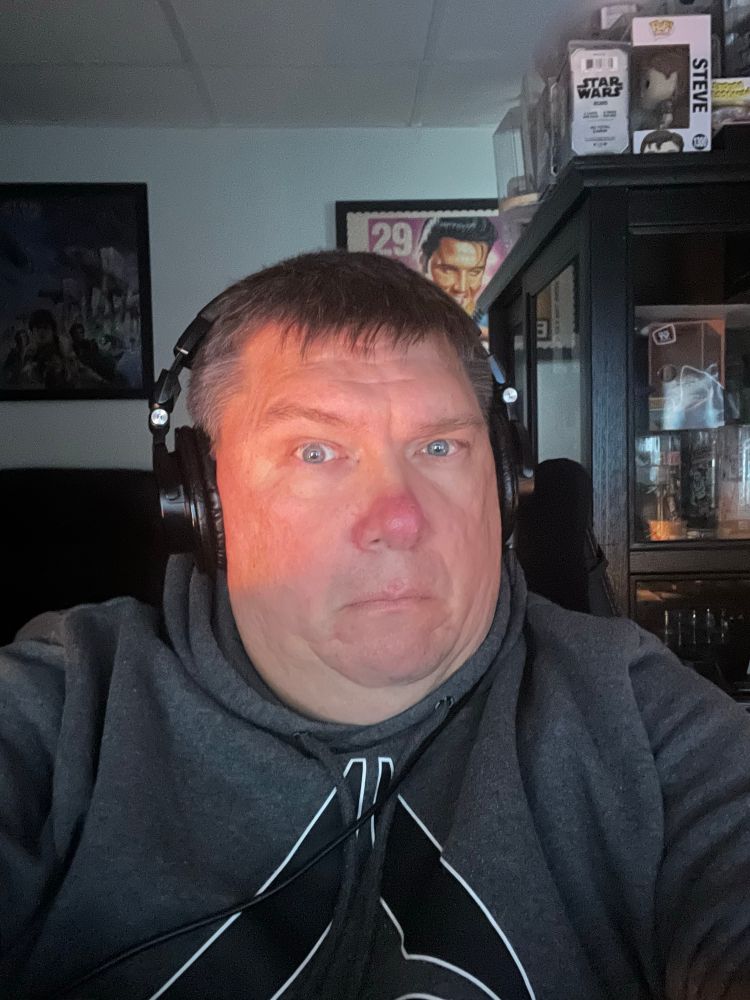 A former cybersecurity elder turned auditor, face washed on the glow of candles, lurks in a cave that is several millions dollars short of being the Batcave. He has a raised eyebrow and a puzzled looked on his face and is dressed comfortably in a grey hoodie.