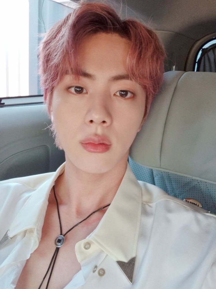 Jin selfie in the backseat of an SUV. His shirt is open showing off a bolo tie. He looks like a hussy with his tits out. 