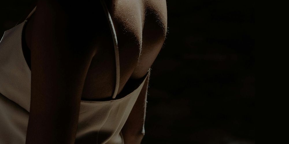 ID: Photo, closeup on a black womans back in the dark. She wears a white dress