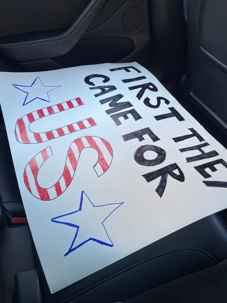 Protest sign in the back of a car: “first they came for us”