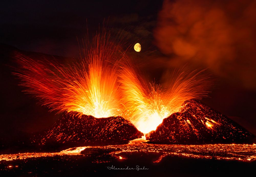 A photo of the Moon rising directly over an erupting volcano, with lava fountains and flows out the front. 