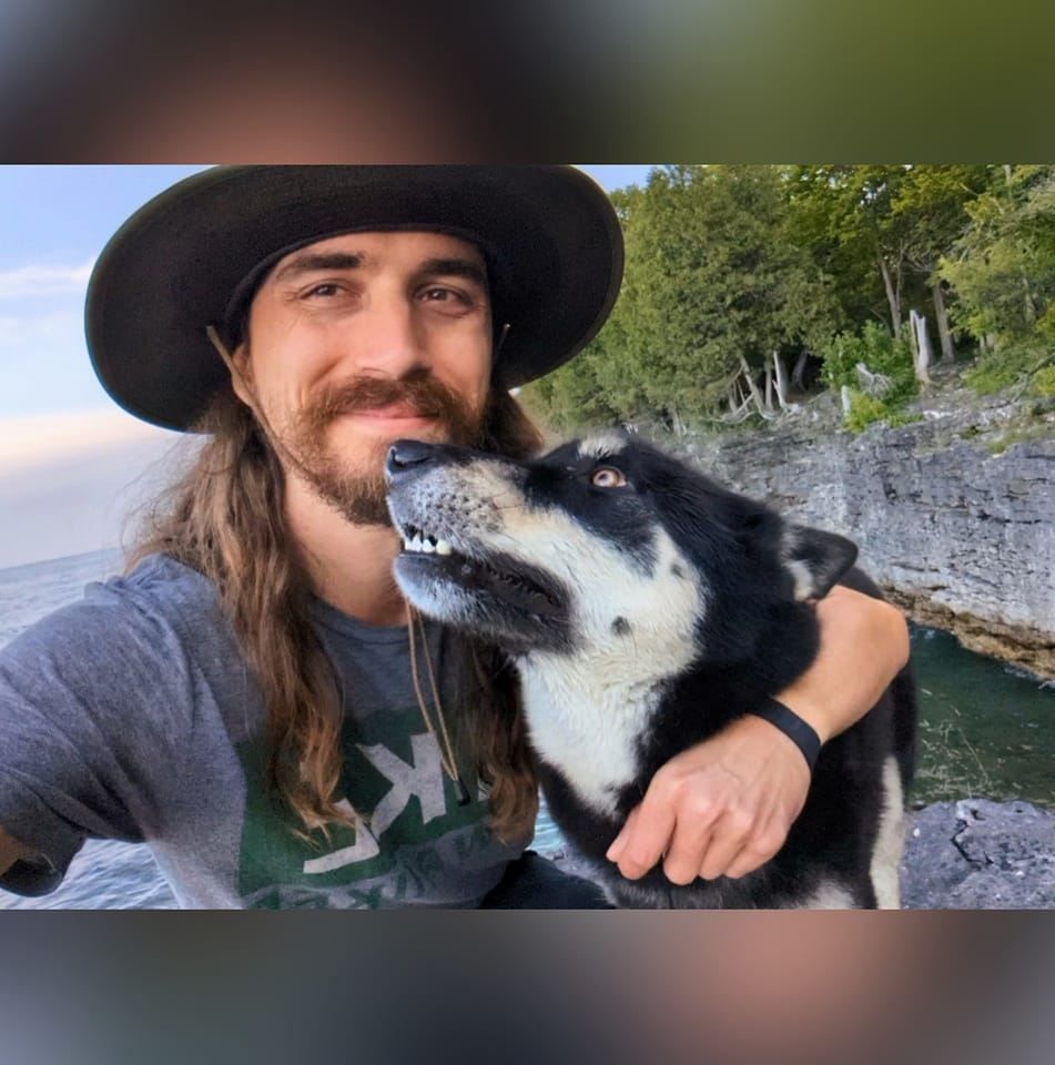 A selfie while crouched down along a rocky lakeshore with my dog looking up at me for kisses.