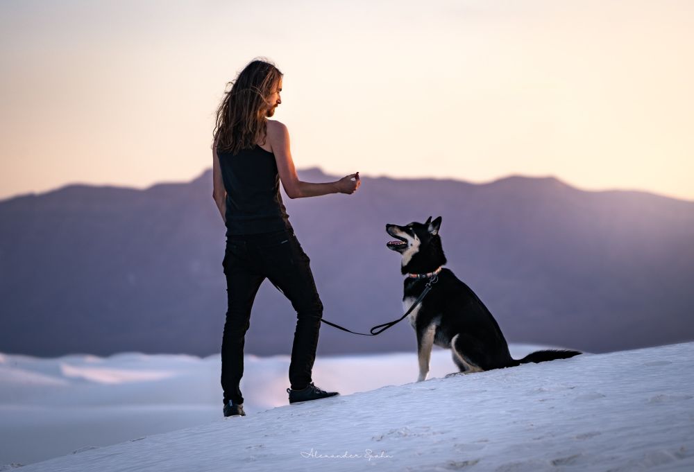 A photo of me holding a treat while my dog sits nicely among the white sands of, well, White Sands.