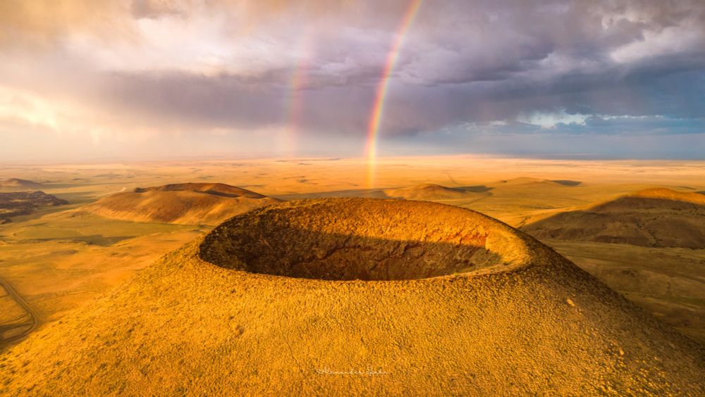 A drone view of a double rainbow over the crater of SP crater (a cinder cone volcano) at sunset.
