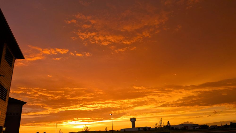 A photo of the sky full of clouds illuminated in vibrant hues of orange at sunset