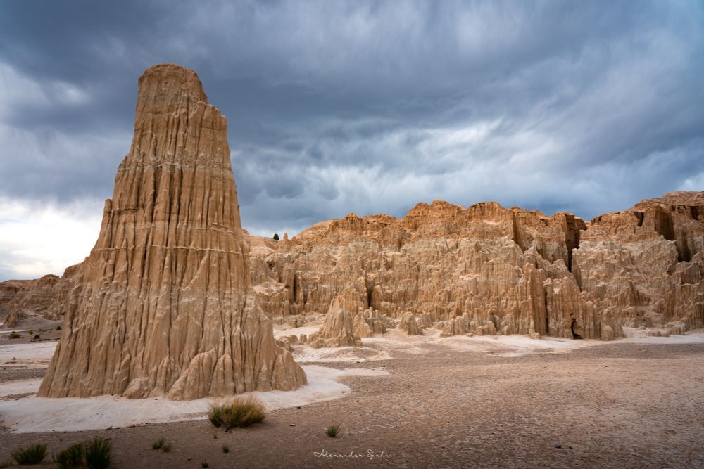 A cathedral of eroded bentonite clay, with a tall tower in the foreground, below a clouded, stormy sky.