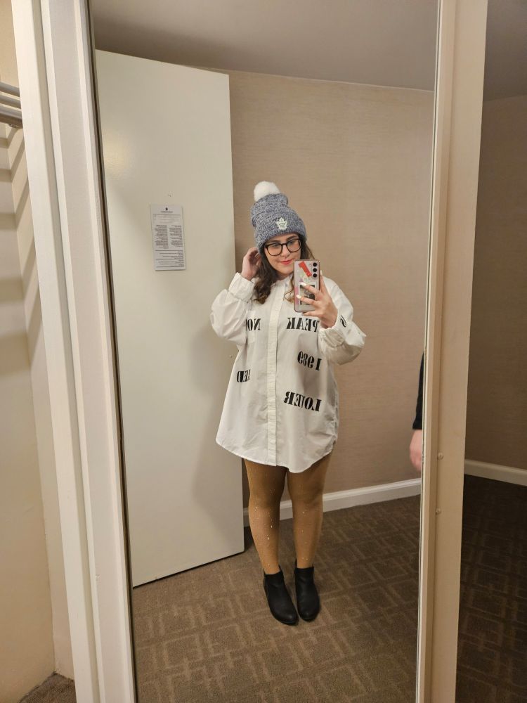mirror selfie. girl (me) with brown hair wearing black booties with oversized white shirt with Taylor Swift eras in black lettering, along with a blue and white maple leafs beanie