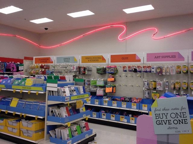An image of the school supplies section of a Target, taken back when Target had neon lights on the walls. In this section can be seen notebooks, glue, art supplies, pencil pouches, scissors, and more.