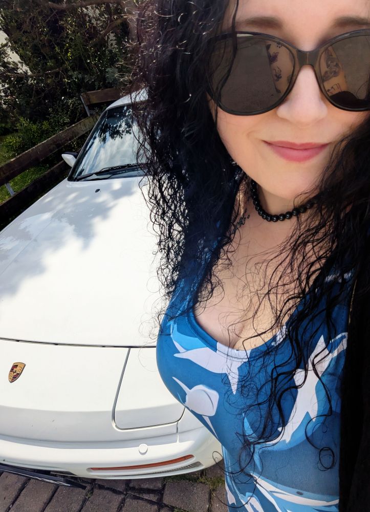 Selfie von mir. Ich trage eine Sonnenbrille und mein Haifischkleid von der Trauerfeier. Im Hintergrund sieht man den alten Porsche meines Vaters. Was man nicht sieht: Wie ich mit etwas feuchten Augen mit heruntergelassenen Fenstern und lauter Musik (Smoke on the water) an der Unfallstelle vorbeigefahren bin.