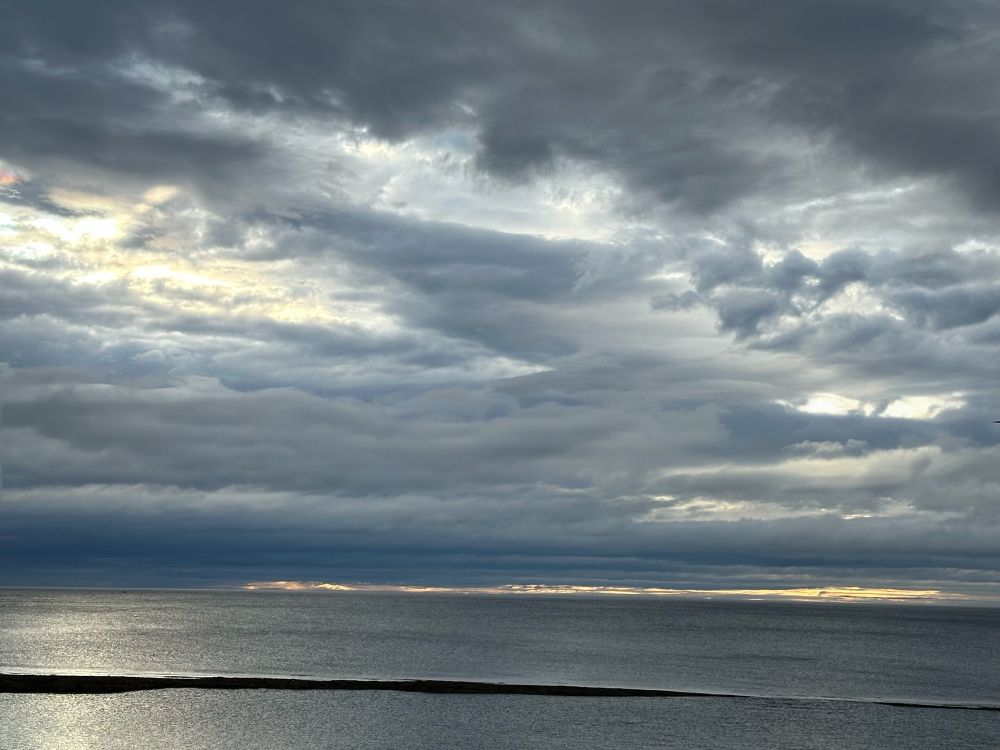 Sun trying to break theough heavy sky, over glass-like sea.