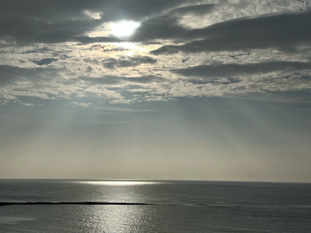 Crepuscular rays fan out from the sun, over a flat sea