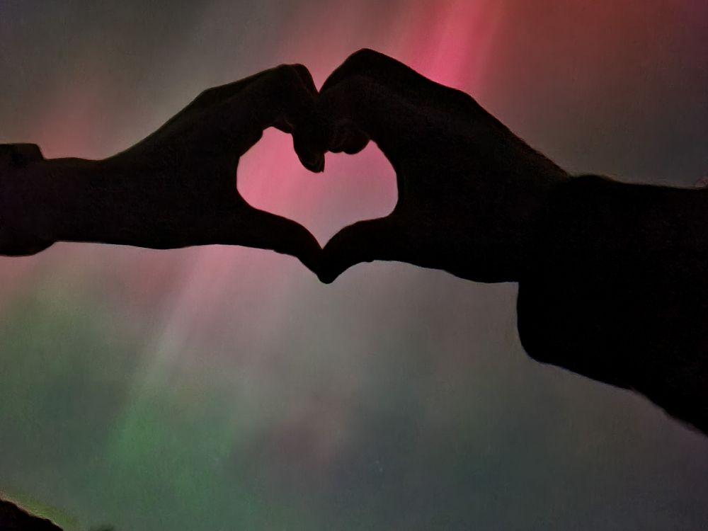 Hands in a heart shape with the northern lights in the background.