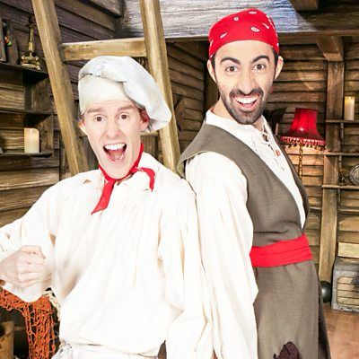 Two young men dressed as very preschool level pirates (their show was on CBeebies). One is wearing chefs whites with a red neck tie (Cook), the other is in a more standard brown pirate tunic with a red head scarf and red belt (Line).