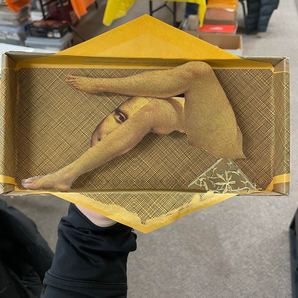 A shallow diorama box with a yellow envelope background with legs and Mona Lisa’s eye attached. A monochrome collage by Katie blake for a Special Agent Collage Collective art call benefiting Collage-O-Rama 