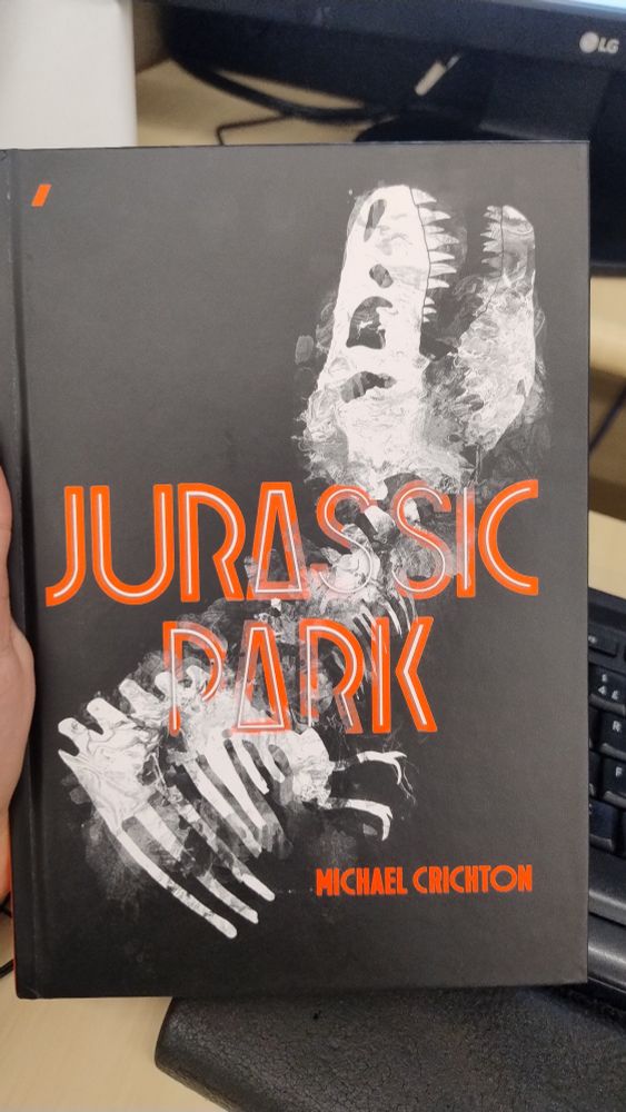 Capa do livro Jurassic Park, de Michael Crichton. Capa preta, com um esqueleto de dinossauro atrás em branco. O título é vermelho