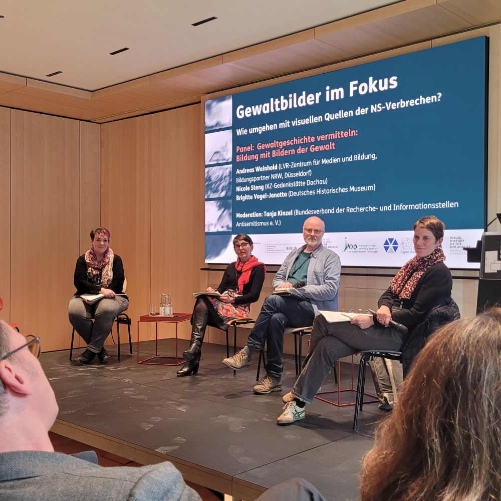 Auf dem Podium sitzen von links nach rechts die im Post genannten Personen, im Hintergrund auf dem Großbildschirm der Titel von Tagung und Panel.