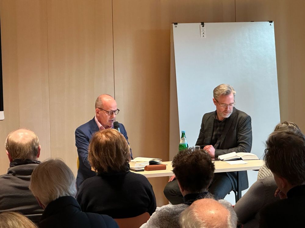 Jens Bisky am Tisch sitzend, mit Handmikrofon, vor sich ein Buch