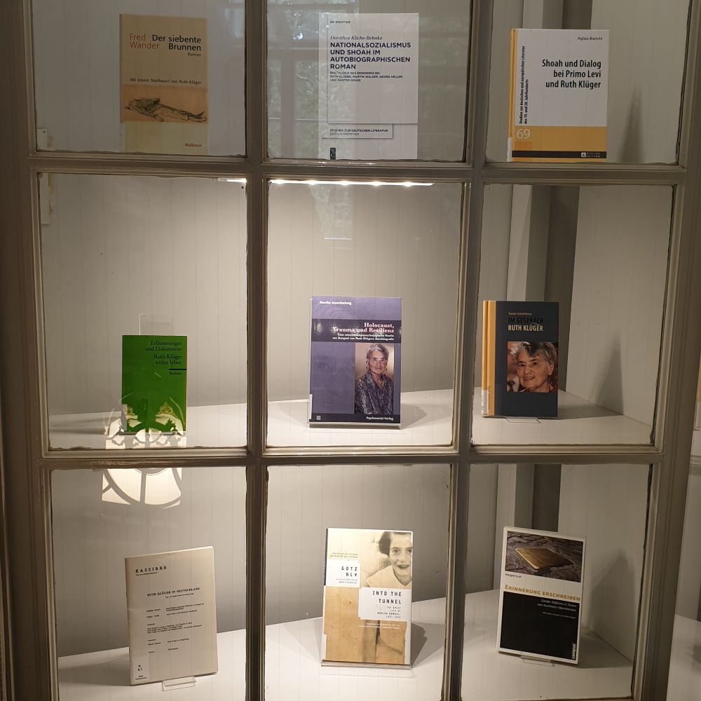 Neun Bücher von und über Ruth Klüger stehen in einem beleuchteten Schaufenster auf drei Regalbrettern übereinander mit jeweils drei Büchern.