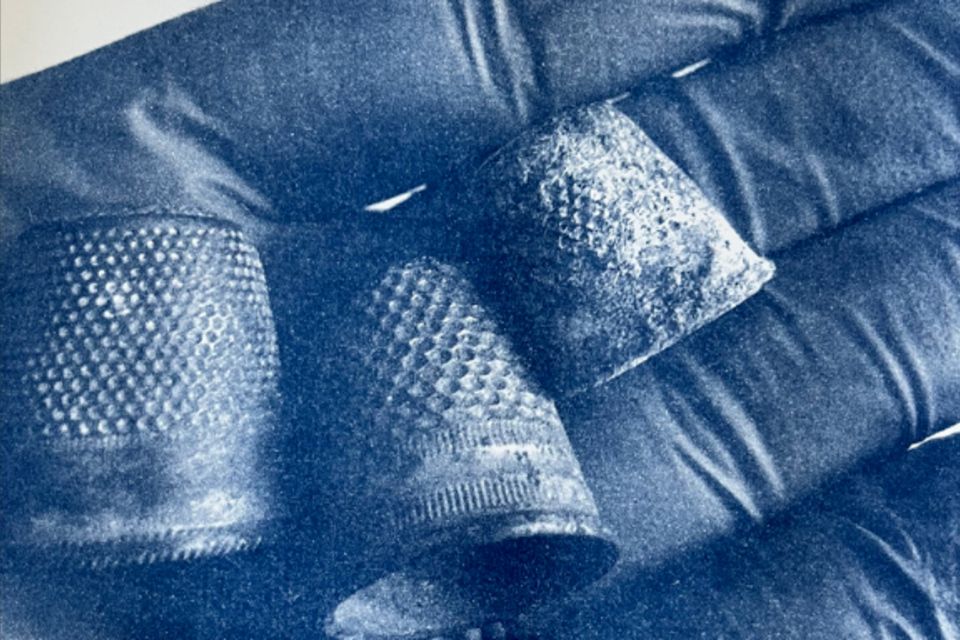 In einer mit einem Latex- oder Gummi-Handschuh bekleideten Hand liegen drei alte Fingerhüte.