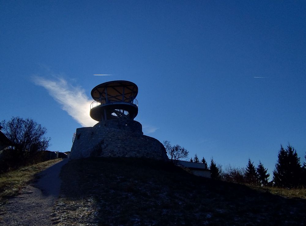 Die dunkle Seite des Fürstenstand auf dem Plabutsch, dahinter Sonne, eine Cirruswolke, ein Kondensstreifen und jede Menge blauer Himmel 