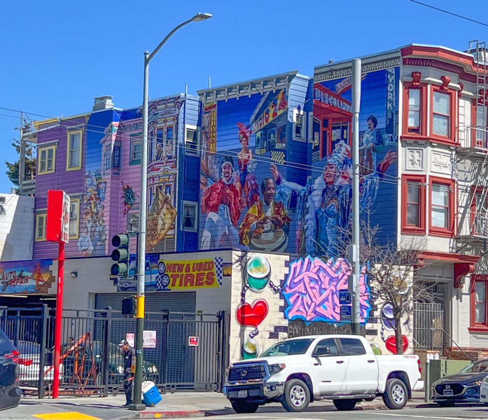 A colorful mural on the side of a building on 24th Street in San Francisco's Mission district.  It depicts scenes and characters from the neighborhood.