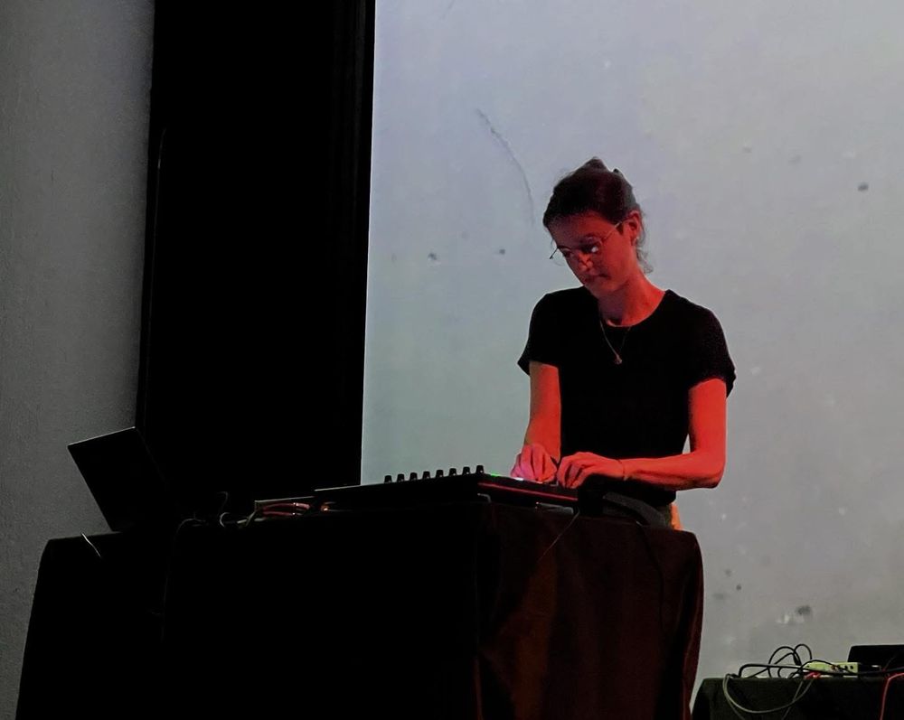 Woman standing at a table with a laptop and electronic music gear.