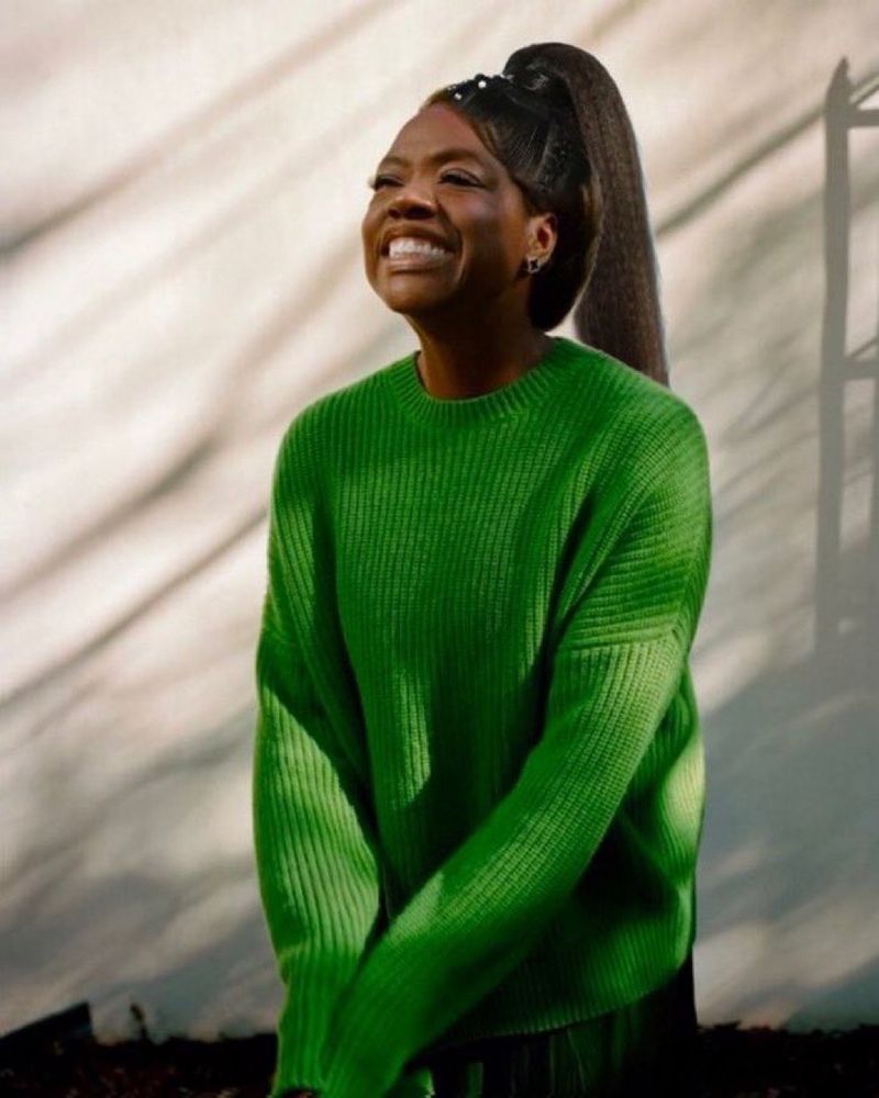 Viola Davis cheesing extra hard in a yaki Ariana Grande ponytail and a green knit sweater with the sleeves covering her hands