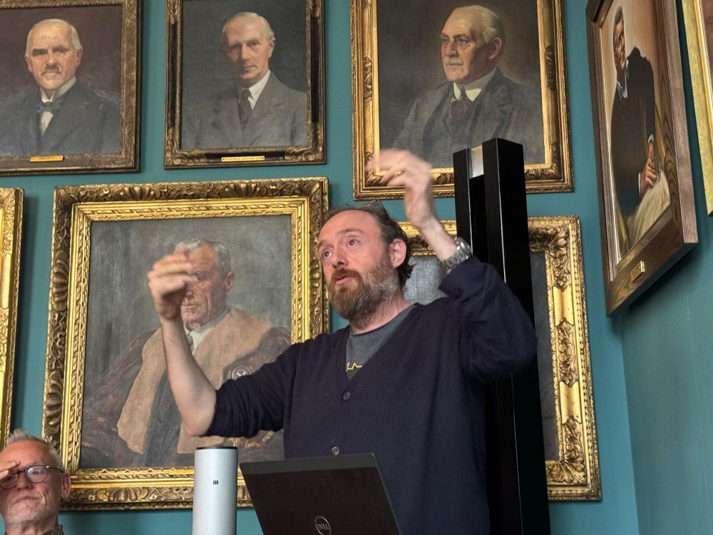 Artist Mitch Miller speaking in front of a wall of portraits of former RIAS presidents.