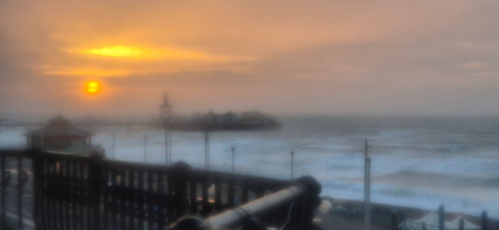Low orange sunrise over the East pier in Brighton, with a rough sea in front, seen through a fuzzy wet window