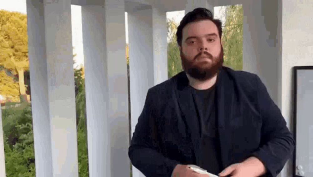 a man with a beard is standing in front of a white railing and holding a cell phone .