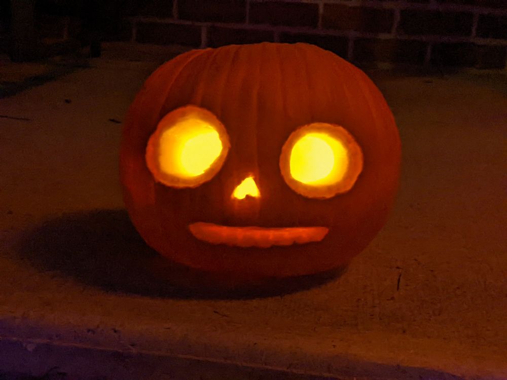 A jack-o'-lantern with large round eyes and grinning teeth glows orange at night 