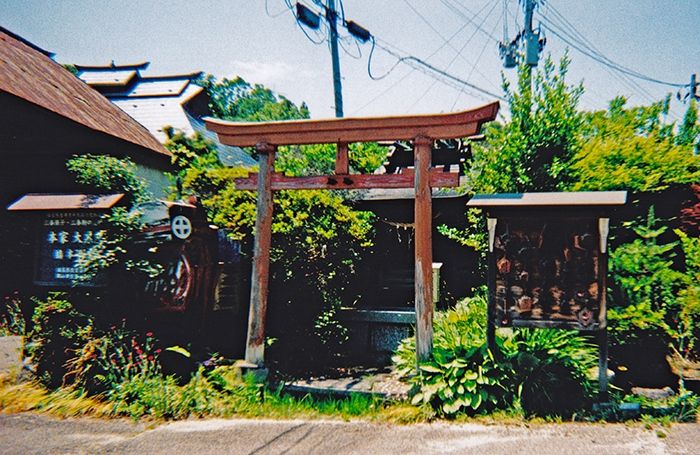 Un torii rouge jiste devant un mini sanctuaire.