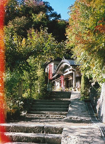 Escaliers en pierre bordé de verdure, au bout un temple blanc avec des drapeaux rouge verticaux.