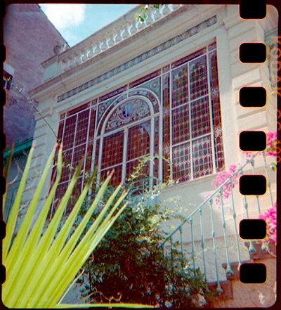 Une grande baie vitrée en fer ouvragé avec pleins de morceaux colorés façon vitrail.