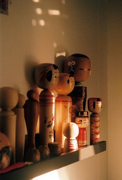 Des kokeshi sur une étagère, éclairée par un soleil couchant.