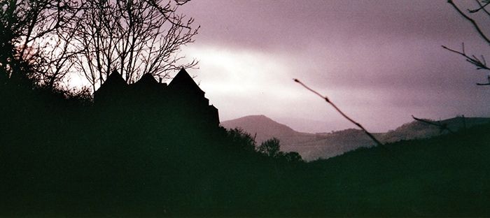 Il fait à peine jour et on voit un paysage de colline, sur la gauche la silhouette d'un gros château massif avec plusieurs tours se découpe.