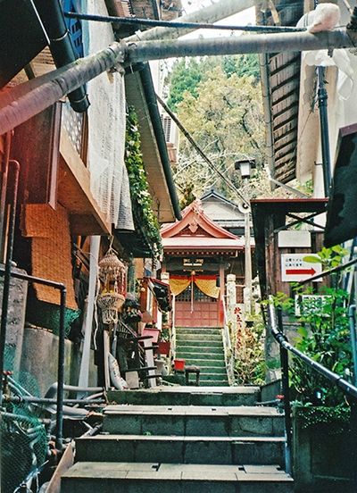 Petite ruelle en escalier en zone urbanisée. Au fond au bout de l'escalier un petit sanctuaire rouge.