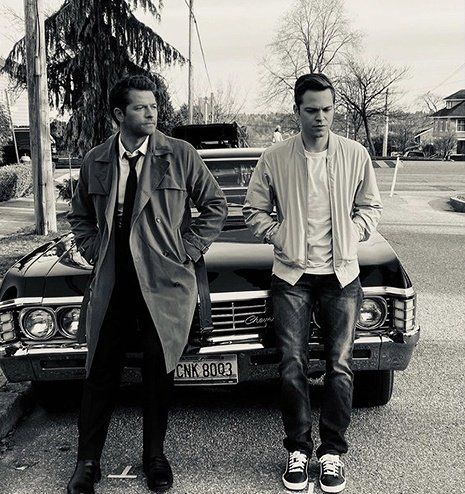 Black and white picture of Castiel and Jack leaning back on the front of Baby (Dean's '67 Impala)
