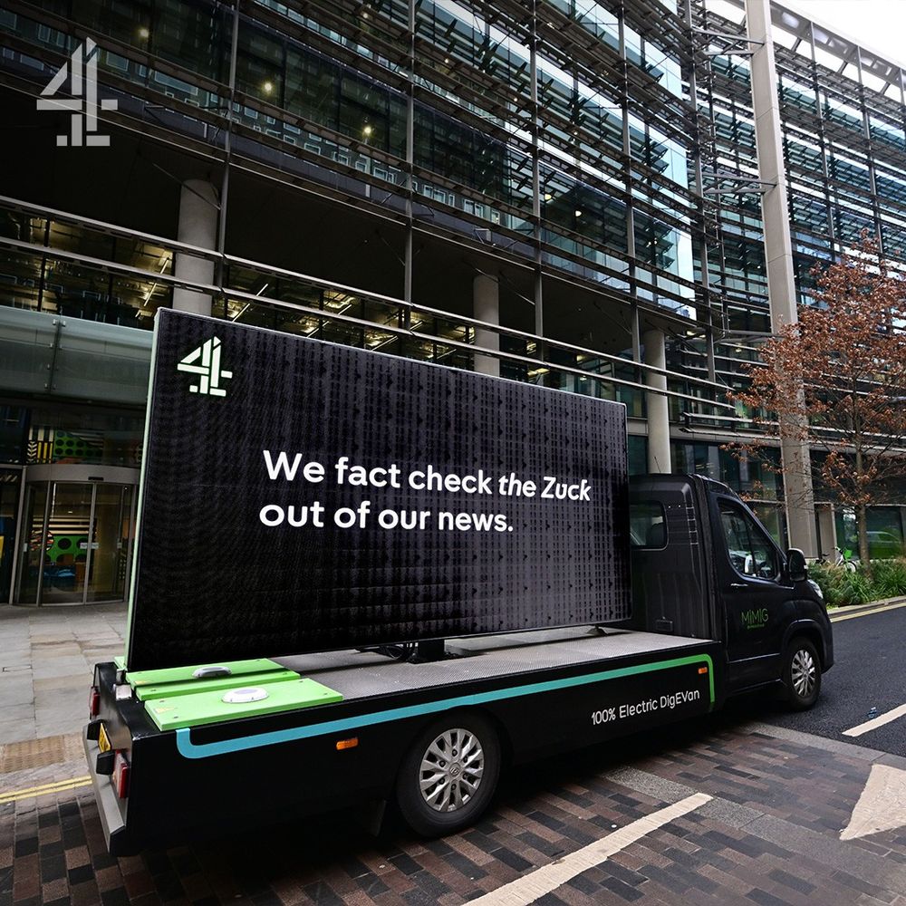 A van is parked on a street outside a big expensive looking building. The building is Meta Headquarters and the Van has a large black sign on the side with the words ‘We Fact Check The Zuck Out Of Our News’ written on the side in the channel 4 font with a channel 4 logo.