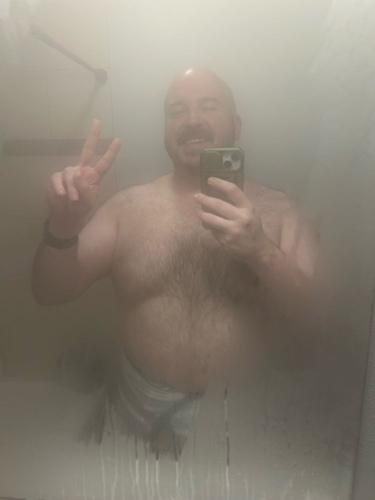It’s a hot dad bod in a steamy shower mirror from the waist up giving a peace sign with a beautiful smile