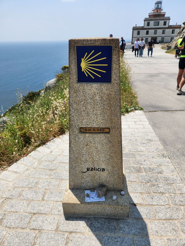A marker bearing a yellow seashell on a blue border at finesterre announces the finish to the camino trail at 0.000 kilometers