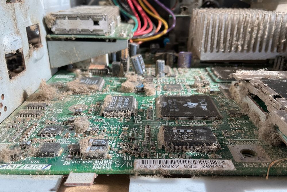 the motherboard of a compact computer, where dust has been forced into every nook and cranny through negative pressure from the fan. the dust is tar sticky and clumped everywhere
