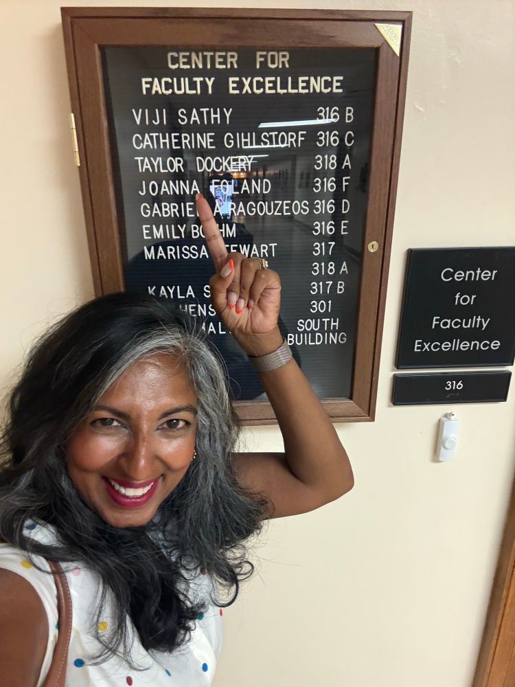 Image of me in front of a sign that lists everyone’s name and office number in the center 
