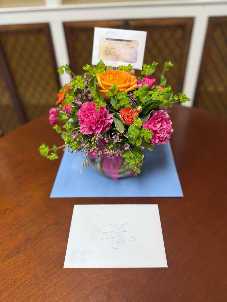 Photo of colorful bouquet on table with a card. Colors are pink and orange shades