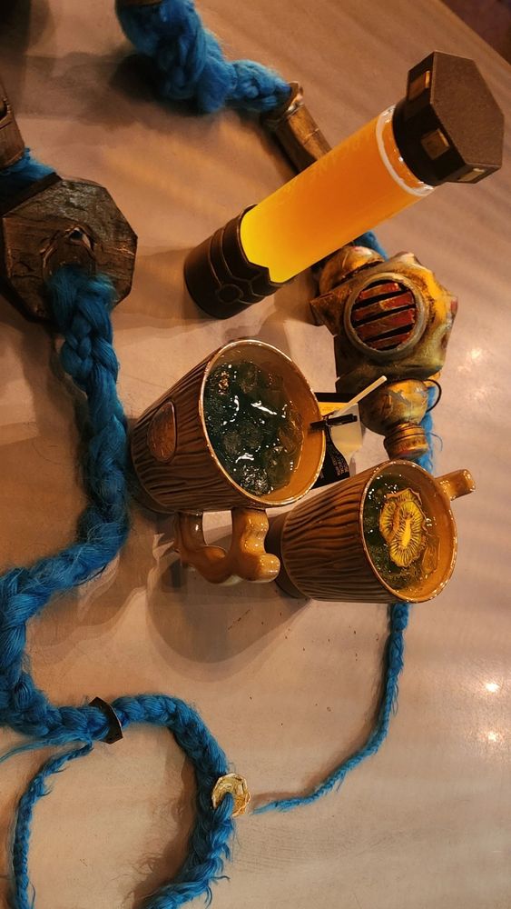 Jinx braids and mask surrounding Arcane themed drinks. 2 in Last Drop style mugs and 1 in an orange shimmer vial