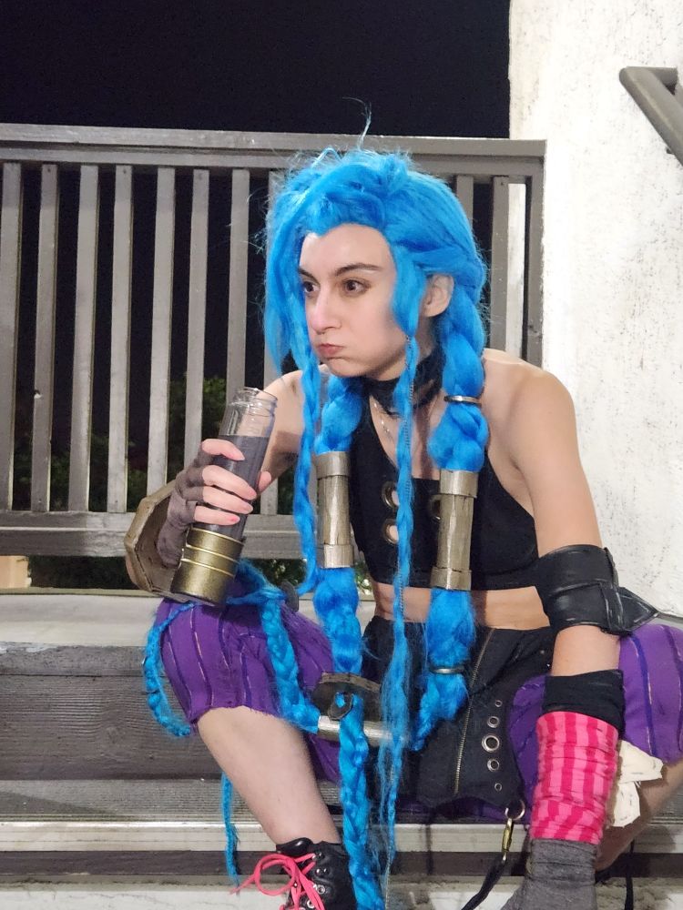 Jinx cosplayer sitting on stairs with a mouthful of a drink that looks like shimmer
