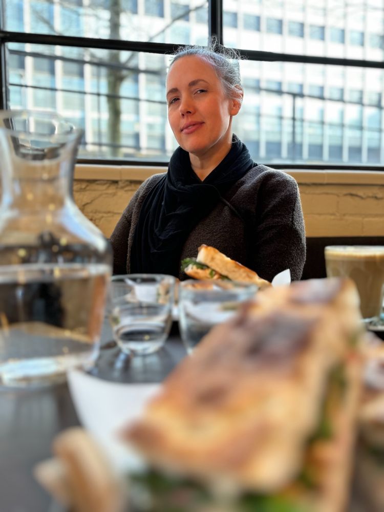 Beautiful woman in a cafe sitting on the other side of a table with sandwiches and glasses of water on it 
