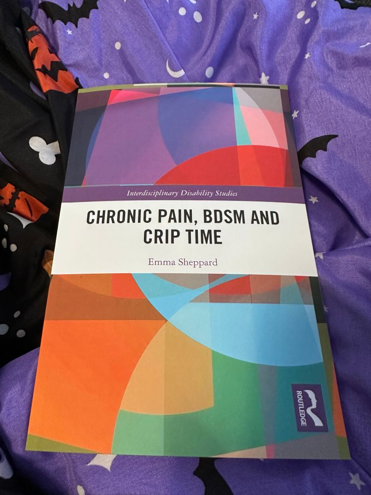 An academic book entitled chronic pain, bdsm and crip time by Emma Sheppard laying atop a Halloween blanket